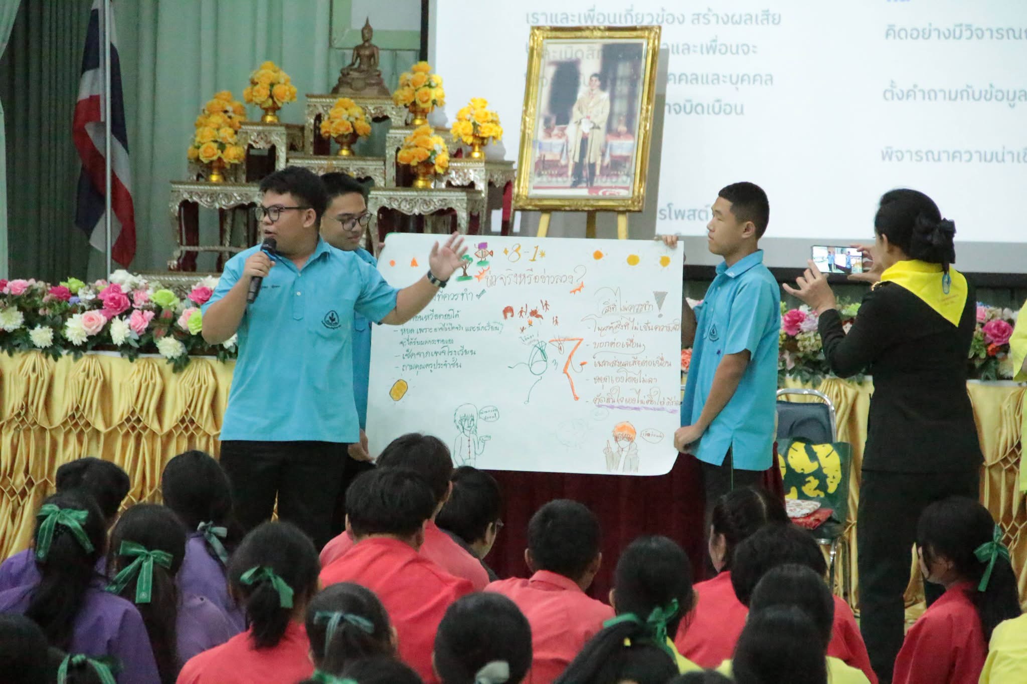 นักเรียนนำเสนอผลงานโปสเตอร์กิจกรรมต่อเพื่อนในหอประชุม